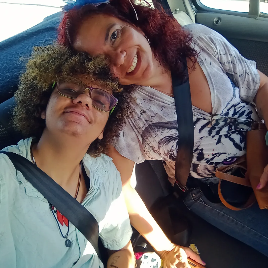Selfie dentro do carro: Vânia sorrindo, de cabelos ruivos cacheados, abraçada ao filho, que usa óculos.